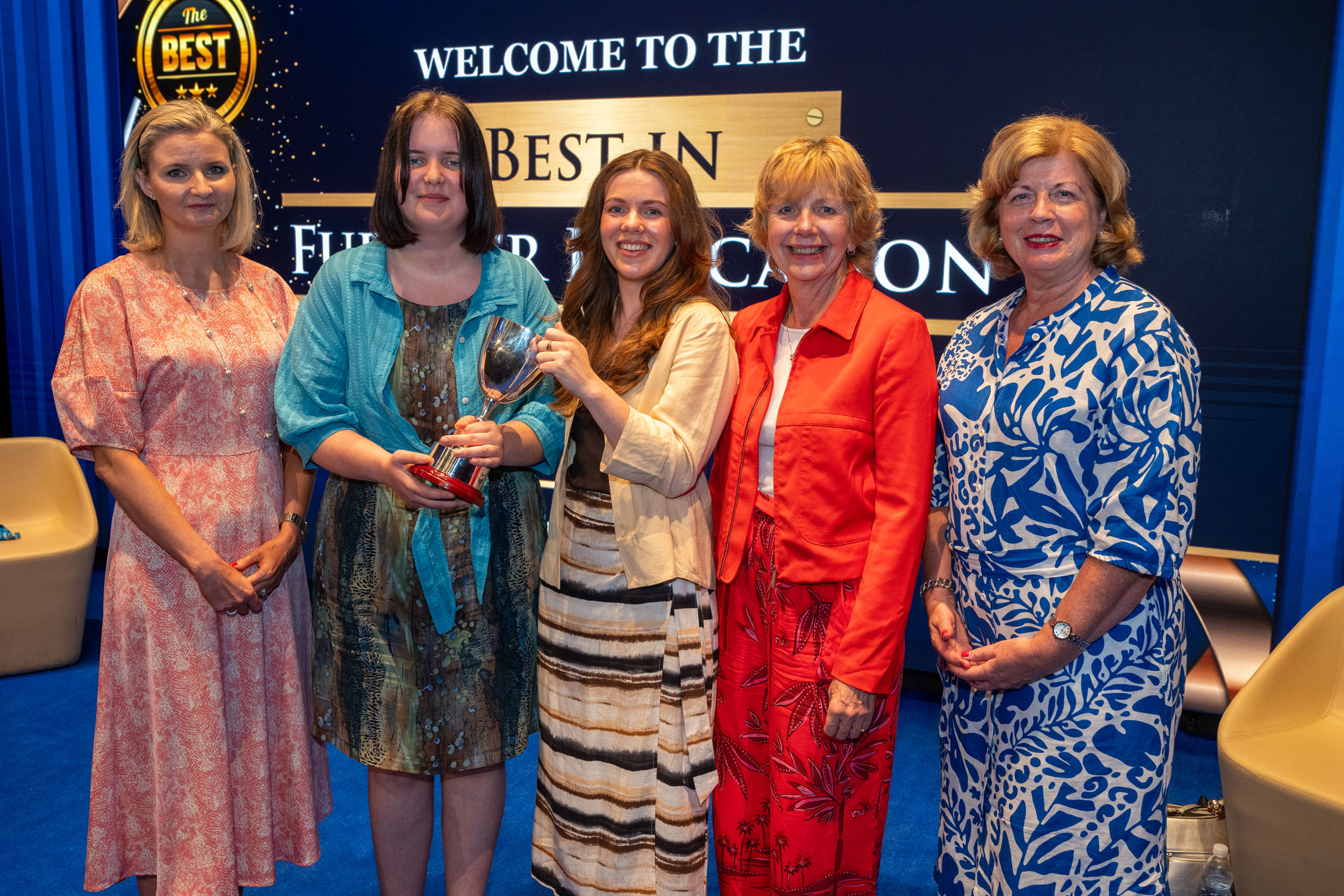 four women in front of Best in Further Education screen. One of the women is presenting a trophy.