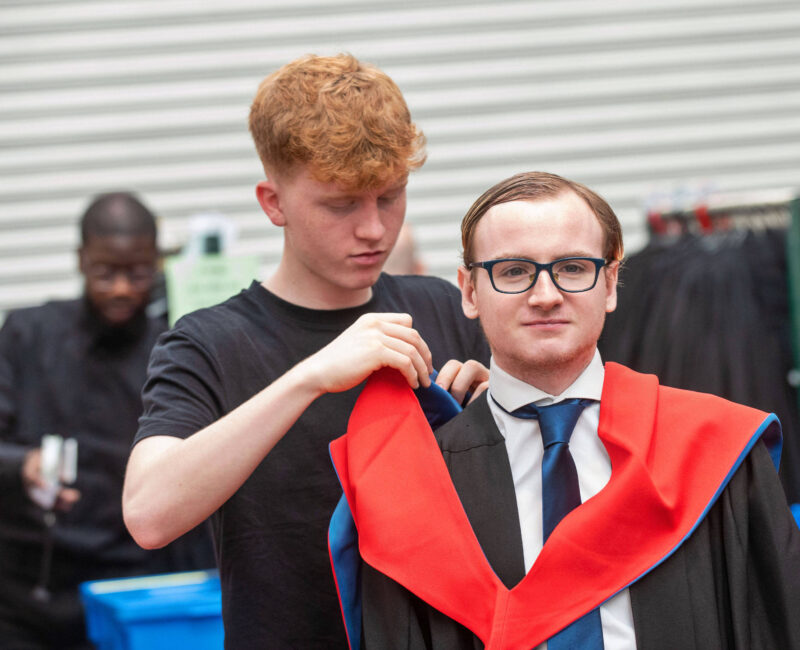 Male graduate has his gown fitted by a member of staff