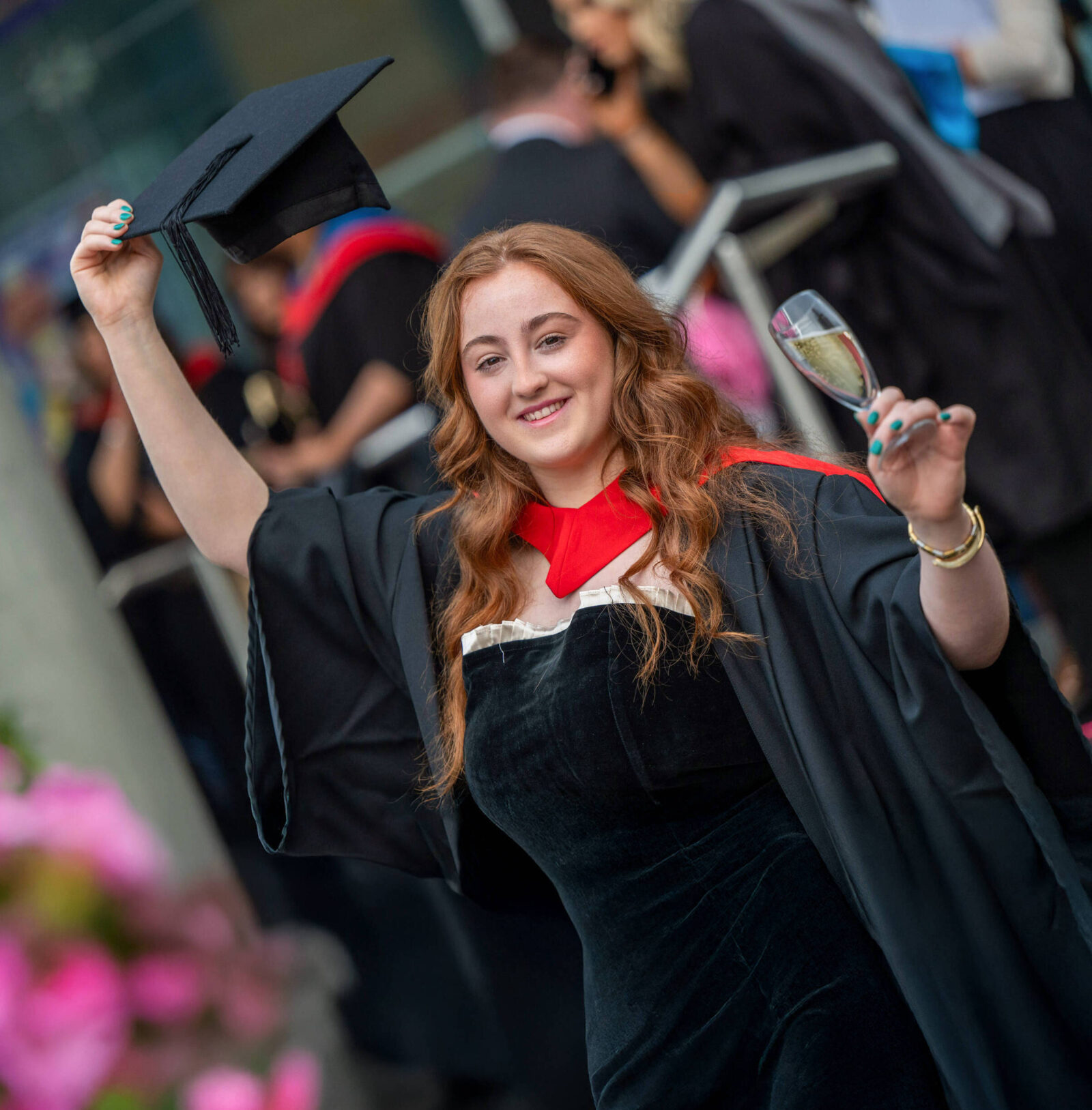 Female graduate raising her cap and holding a glass of champagne