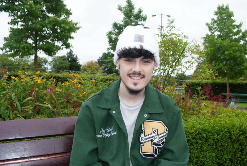 A young man in a white hat sits in a garden. He is wearing a white hat